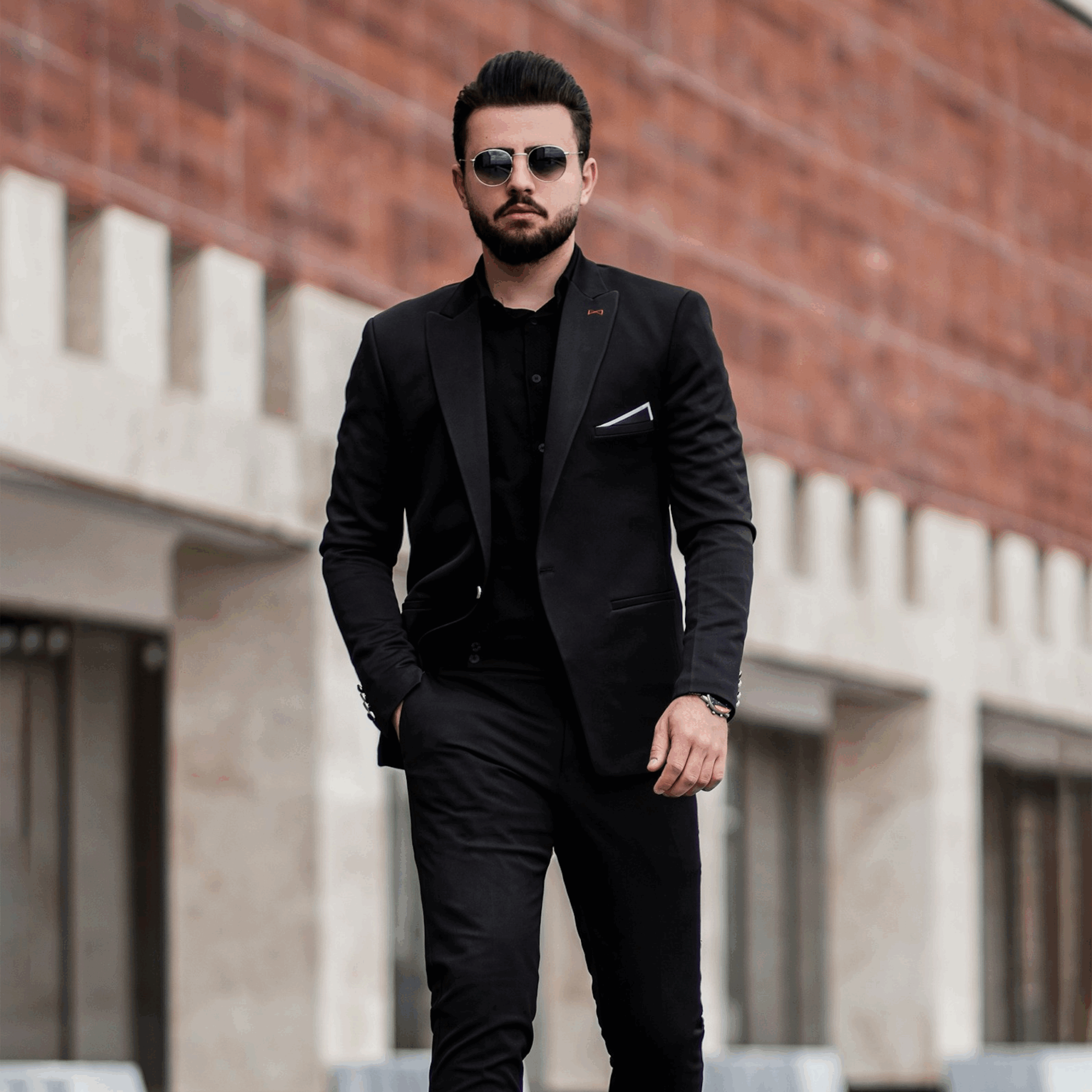 Man wearing an all-black modern suit with sunglasses, walking outdoors.